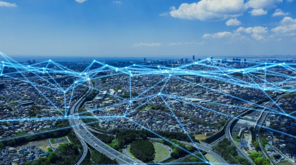 Aerial view of a dense city with glowing blue links strung across rooftops and motorways, mapping mesh coverage.